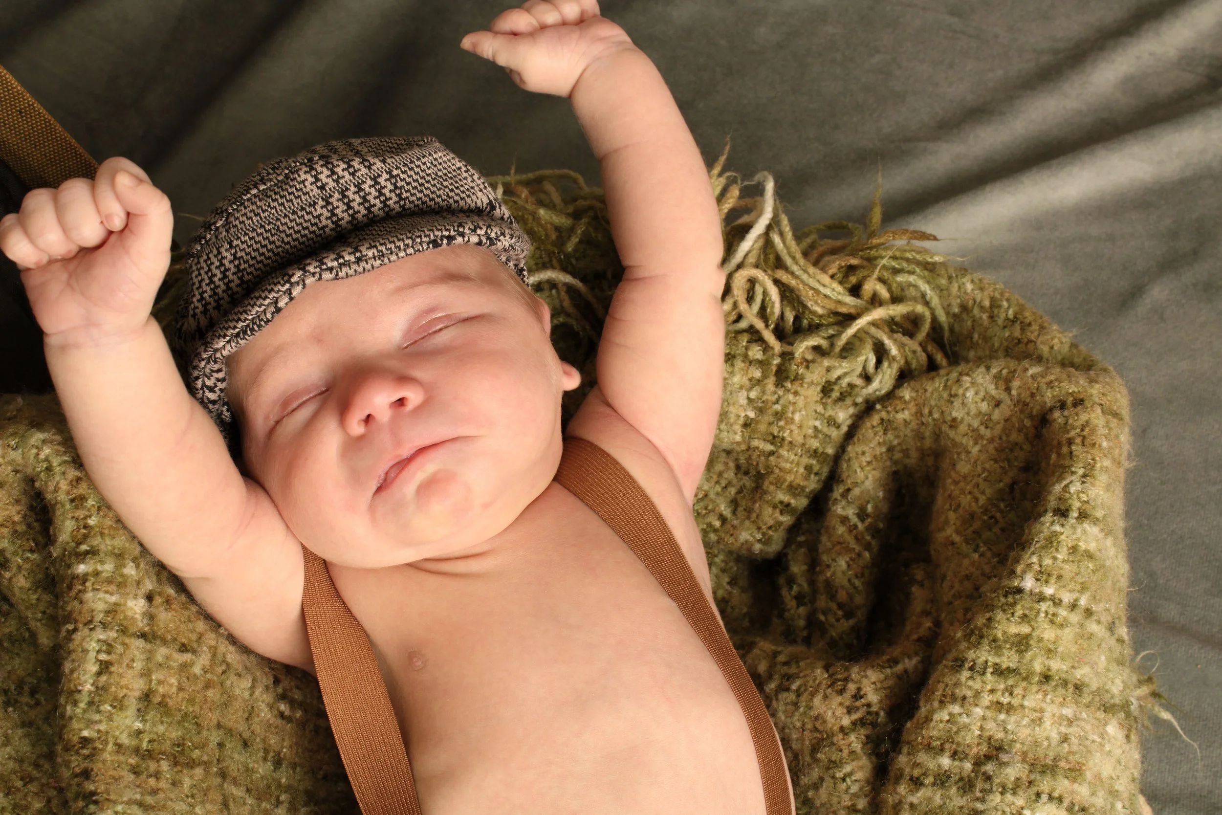 Close-up of a newborn baby boy stretching his arms while wearing a houndstooth cap during a newborn photography session