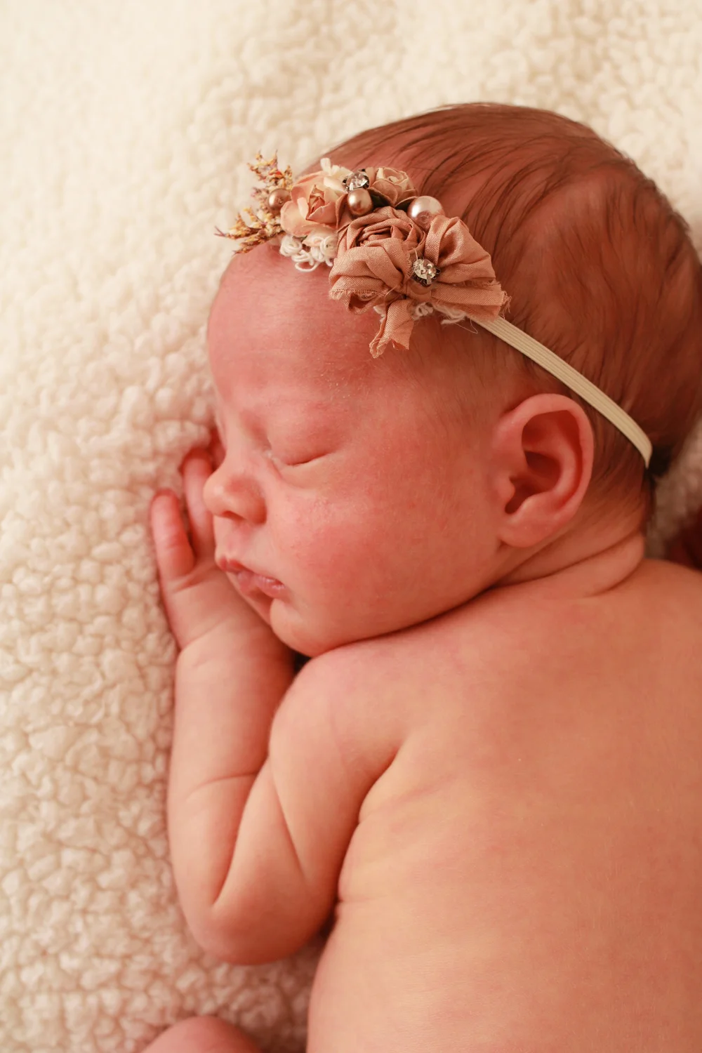 Profile portrait of a sleeping newborn baby girl wearing a delicate floral headband during a newborn photography session